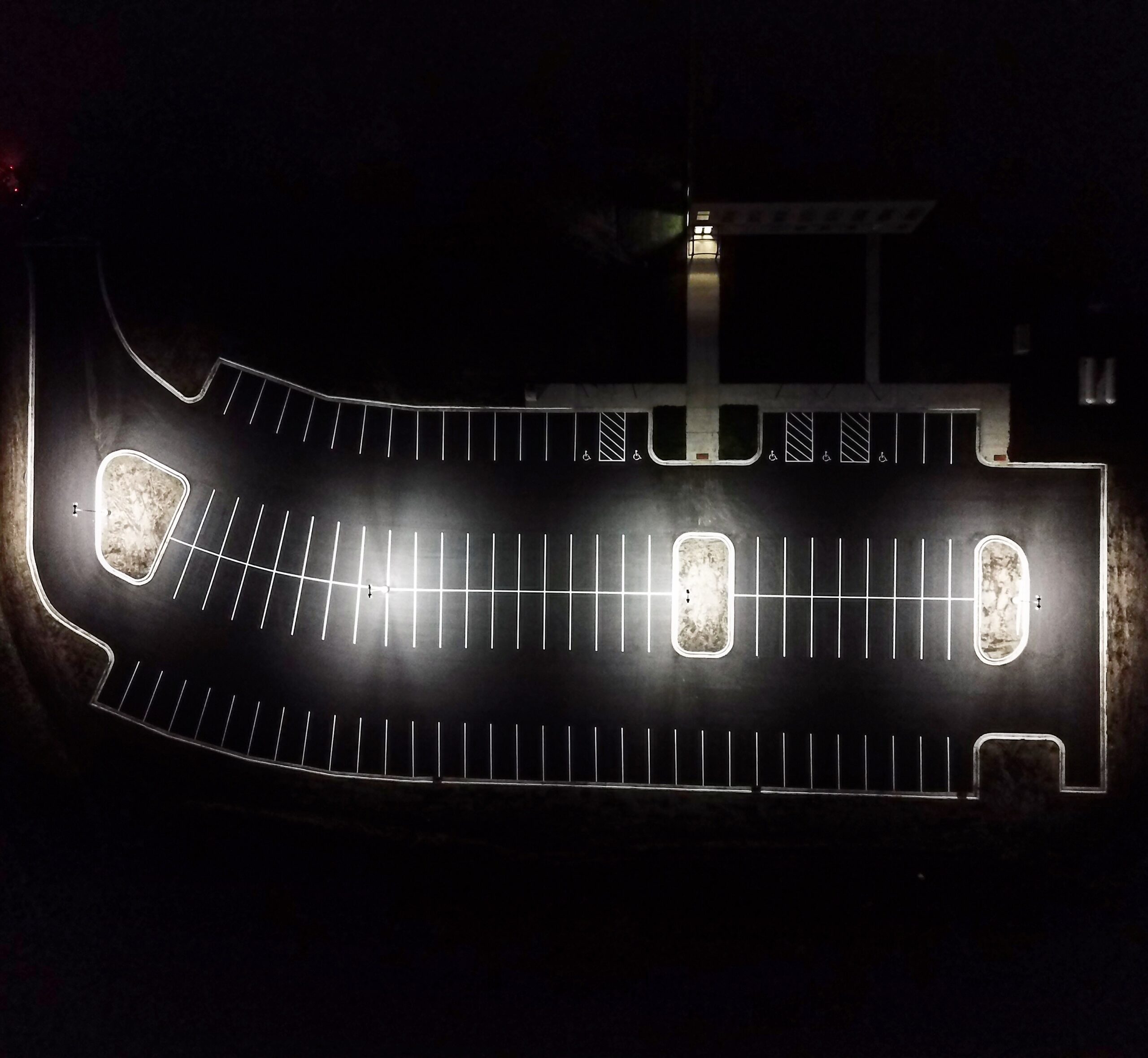 Aerial night view of a freshly striped parking lot with white stalls and accessible markings